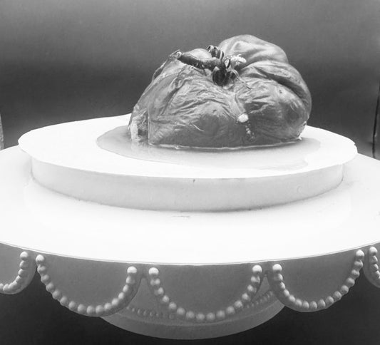 a black and white photo of a rotten tomato on a cake stand